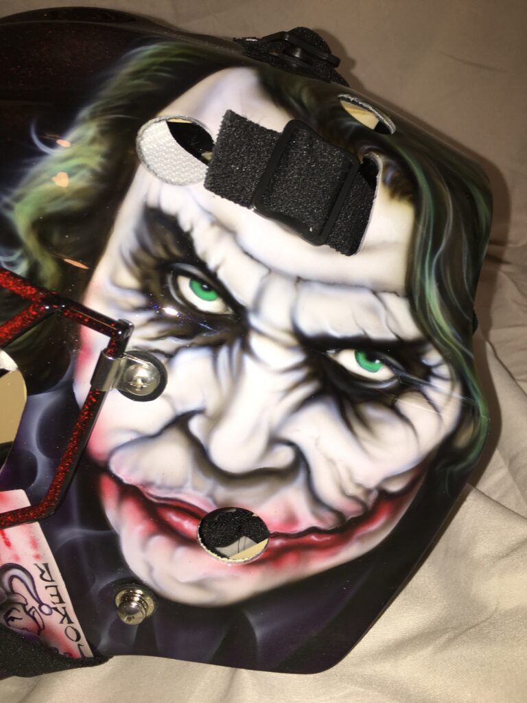 Face painted as a sinister Joker character with intense eyes and a wide smile.