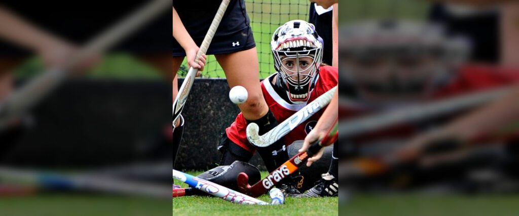 Field hockey goalie in action blocking a shot during a game.