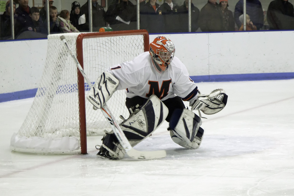 Ice hockey goalie in white and black gear blocking a shot.