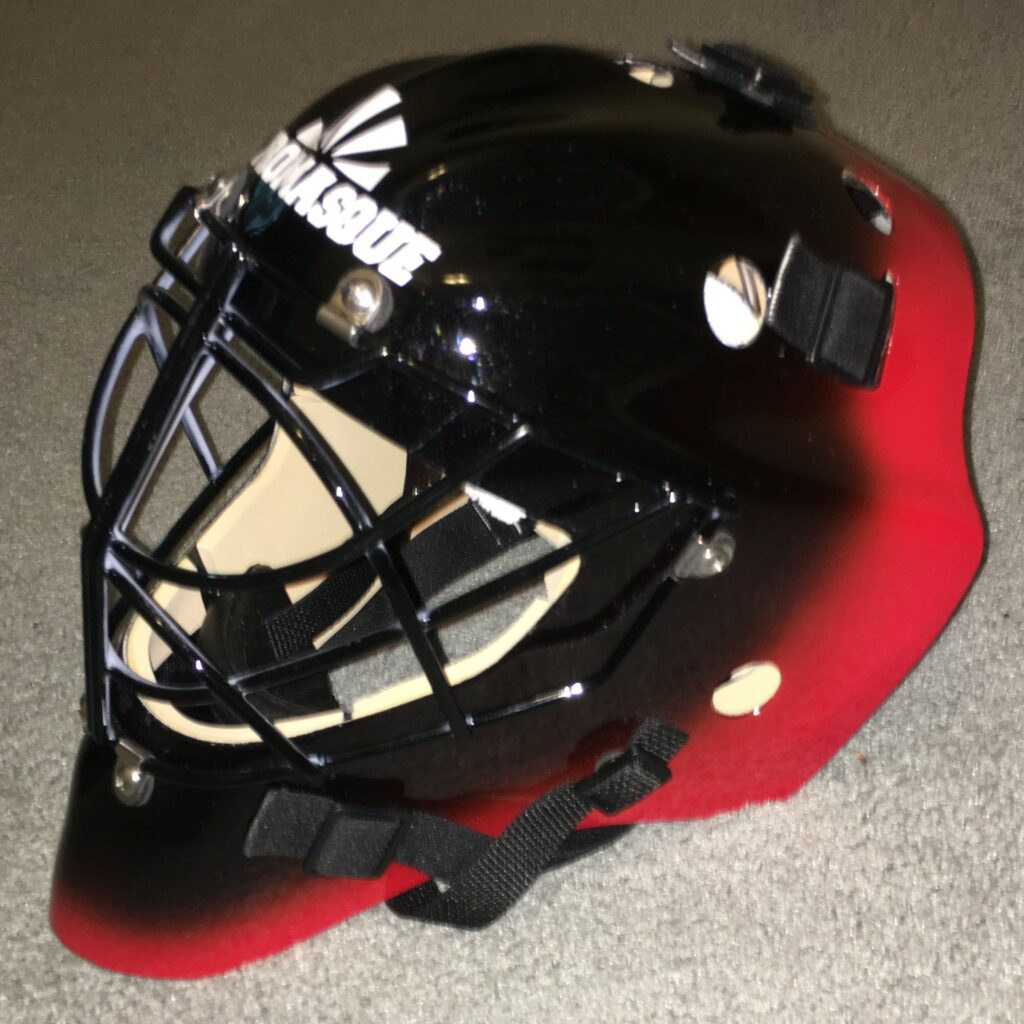 Black and red hockey helmet with cage on beige carpet.