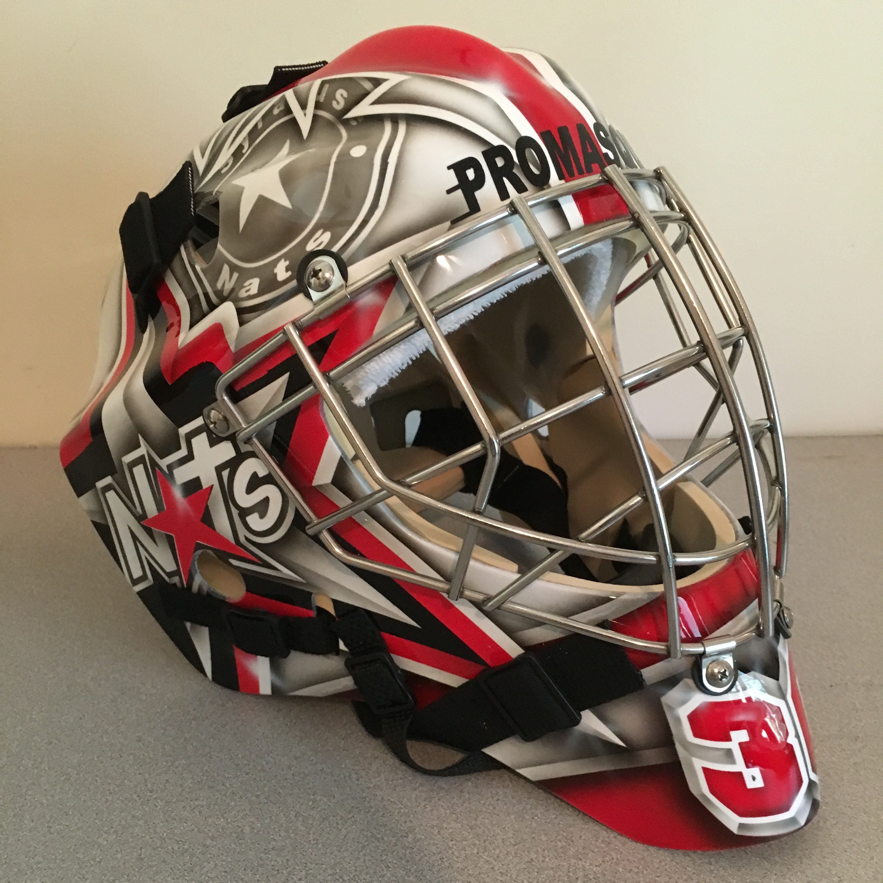 A red, black, and white ice hockey goalie mask with a protective cage.