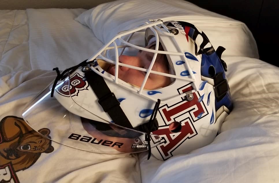 A hockey goalie resting with helmet on.
